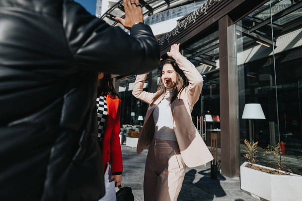 Energiczna młoda kobieta w stylowym stroju świętuje moment sukcesu na słonecznej ulicy miejskiej, ciesząc się z przyjaciół. - Zdjęcie, obraz