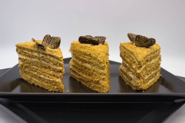 ブラックプレートにチョコレートピースをトッピングした蜂蜜ケーキの3つの層. - 写真・画像