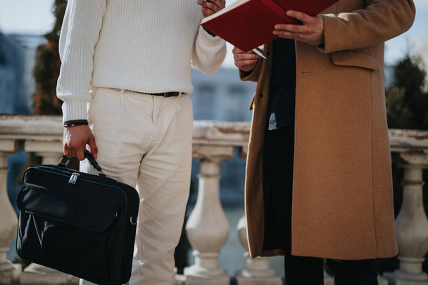 Crop of two business professionals engaging in a casual outdoor meeting, one holding a briefcase and the other holding a red folder. - Photo, Image