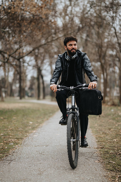 Itsevarma yrittäjä ajaa pyörällä, kantaa salkkua kaupunkipuistossa, työskentelee ulkona puiden kanssa taustalla. - Valokuva, kuva
