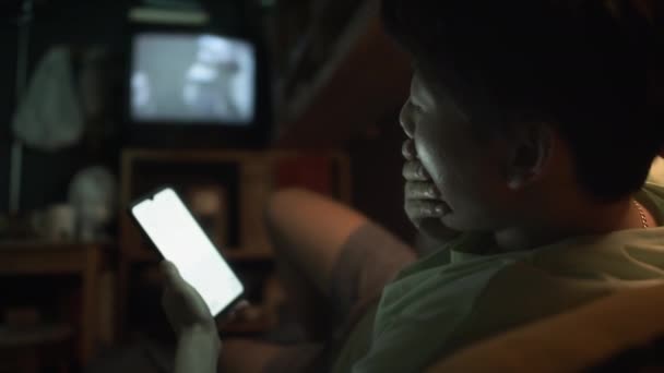 Medium footage of tired young Chinese man using smartphone, bocejo, em seguida, abraçando travesseiro e deitado para dormir na cama, enquanto descansa em casa no micro apartamento após o dia de trabalho - Filmagem, Vídeo