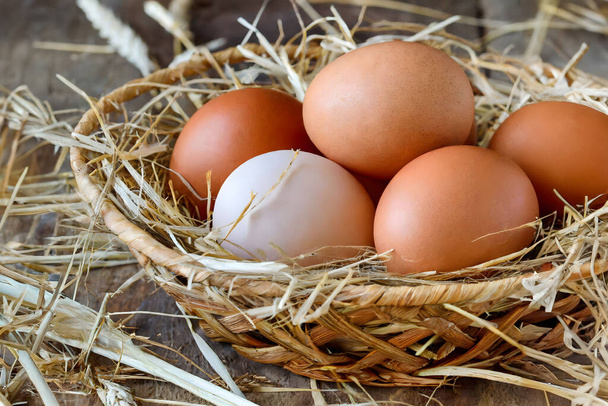 Ένα ρουστίκ καλάθι γεμάτο με φρέσκα, βιολογικά αυγά φωλιασμένα σε άχυρο, αναδεικνύοντας τα φυσικά, από αγρόκτημα σε τραπέζι προϊόντα - Φωτογραφία, εικόνα