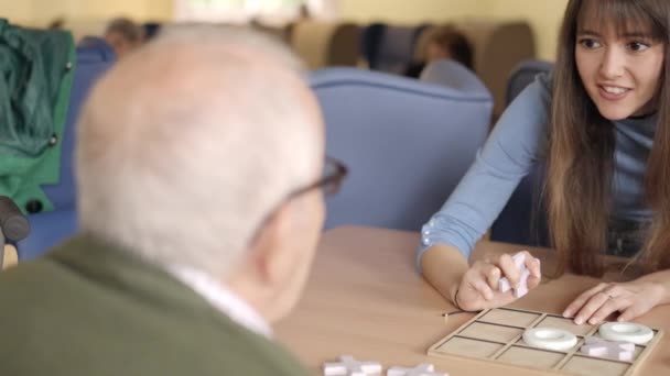 Vídeo en cámara lenta de una chica explicando las reglas de un juego a un hombre mayor en un asilo de ancianos - Imágenes, Vídeo