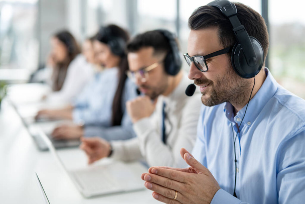 Nahaufnahme Porträt eines gutaussehenden Mannes mit Headset, der seinem Kunden während eines Online-Chats im Call Center erfolgreich Aufgaben löst. - Foto, Bild