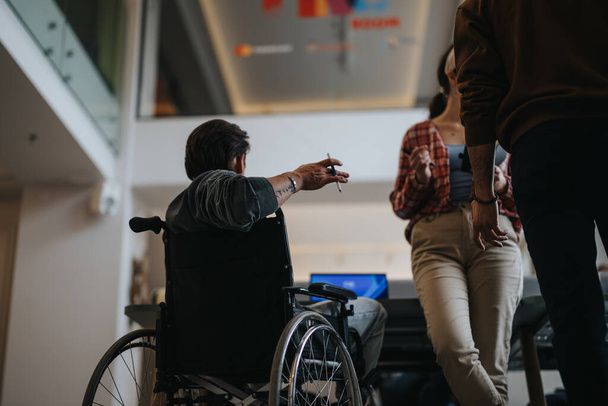 Ein Rollstuhlfahrer nimmt aktiv an einer Teamdiskussion teil und betont Inklusivität und Barrierefreiheit am Arbeitsplatz. - Foto, Bild