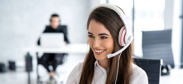 Panoramic view of smiling female call center agent in white headset talking to client at office - Photo, Image