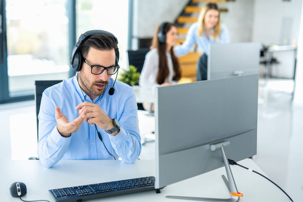 Dedicated male customer service representative communicating with customer trying to provide appropriate solutions for client issues at call center. - Photo, Image