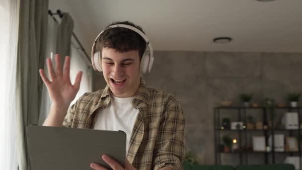 νεαρός άνδρας έχουν βιντεοκλήση χρήση ψηφιακών tablet και ακουστικά στο σπίτι - Πλάνα, βίντεο
