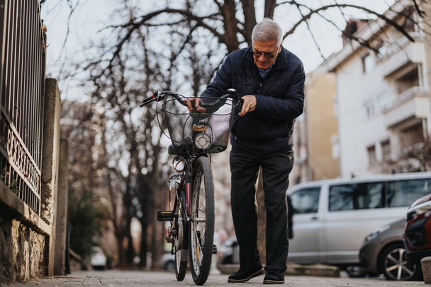 Vanhempi mies tarkistamassa polkupyörää hiljaisella kaupunkikadulla syksyllä. - Valokuva, kuva