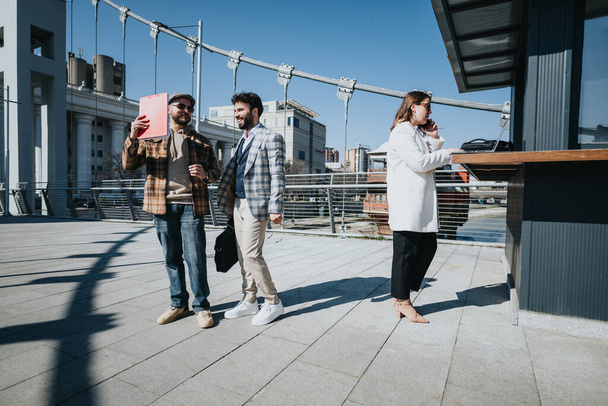 Şehir merkezindeki bir şehirde stratejileri tartışmak için bir tablet kullanan genç iş adamlarının açık havada birlikte çalışmalarının dinamik çekimi.. - Fotoğraf, Görsel