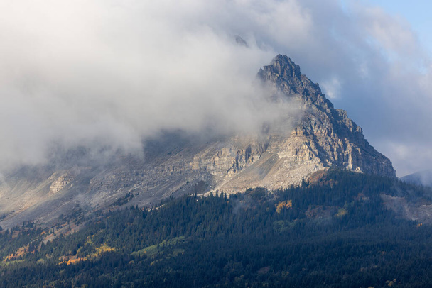 Een berg bedekt met wolken met een rotspiek. De lucht is bewolkt en de berg is bedekt met bomen. - Foto, afbeelding