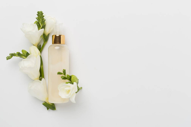Botella cosmética con flores de freesia sobre fondo de color, vista superior - Foto, Imagen