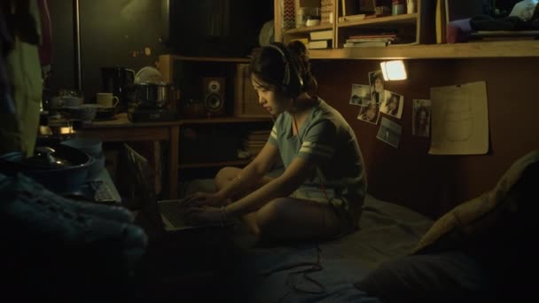 Полный боковой снимок молодой китаянки, сидящей на двухъярусной кровати в обувной квартире, играющей в шутеры на ноутбуке онлайн, проигрывающей турнир, сбрасывающей наушники и вспотевшей от ужаса и гнева - Кадры, видео