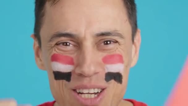 Wideo w studiu z chromą zbliżenia człowieka z egipską flagą namalowaną na twarzy wspierającą egipską drużynę - Materiał filmowy, wideo