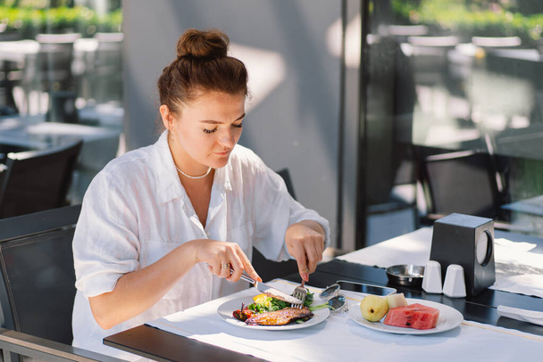 Eine Frau im weißen Hemd isst in einem Café im Freien zu Mittag oder frühstückt. Frau isst gesundes Essen auf Restaurantterrasse - Foto, Bild