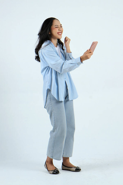 полная длина съемки счастливой азиатской индонезийской женщины, держащей смартфон на изолированном фоне - Фото, изображение