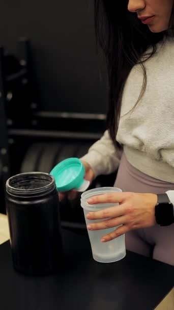 kobieta sportowiec otwiera jej shaker aby dodać kreatynę przed jej trening w siłowni - Materiał filmowy, wideo
