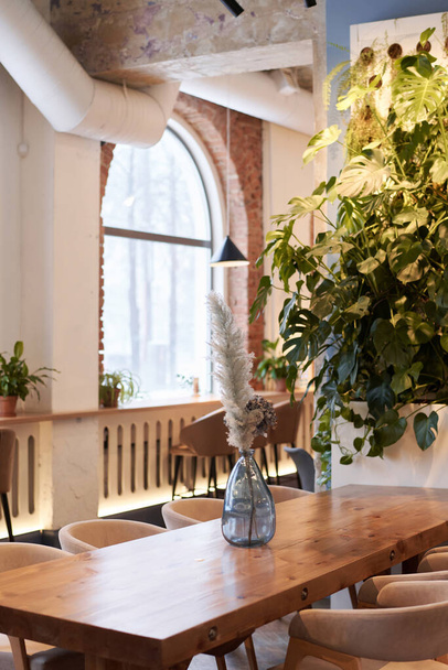Vertikální ne lidé záběr části moderního interiéru restaurace s květinami ve skleněné váze na dřevěném stole, kopírovací prostor - Fotografie, Obrázek