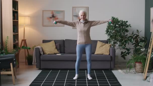 Full stab shot of fit biały senior kobieta robi boczne ramię podnieść ćwiczenia z hantlami podczas treningu w domu w ciągu dnia - Materiał filmowy, wideo
