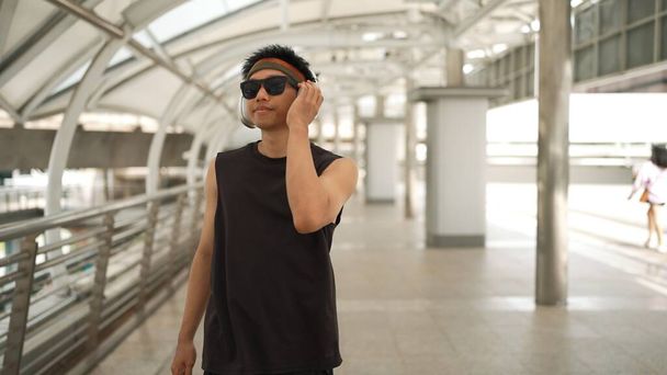 Close-up de dançarino bonito inteligente movendo as mãos enquanto dança a música hip hop. Asiático hipster usando fone de ouvido enquanto caminha ao longo do corredor com fundo borrado. Desporto ao ar livre 2024. Sprightly. - Foto, Imagem