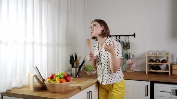 Energinen valkoihoinen äiti laulaa pitämällä kauha moderni keittiö samalla ruoanlaitto ja salaatti aamiaiseksi. Happy House keeper siirtymässä musiikkia samalla valmistautua tekemään terveellistä ruokaa. Pedagogiikka. - Materiaali, video