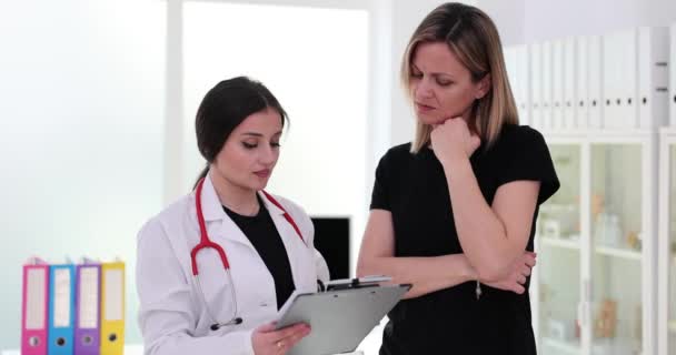 Female doctor anxiously telling sad patient about results of tests indicating disease process. Woman patient listens medic in private clinic - Séquence, vidéo