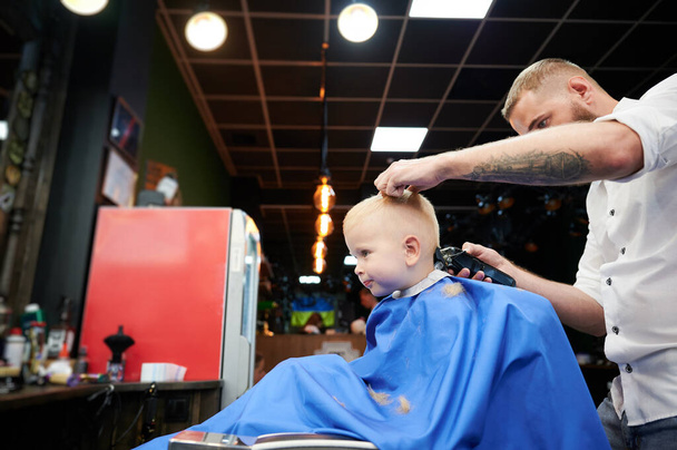 Barbeiro usando pente e barbeador para cortar o cabelo. Cabeleireiro profissional barbear crianças nuca. - Foto, Imagem