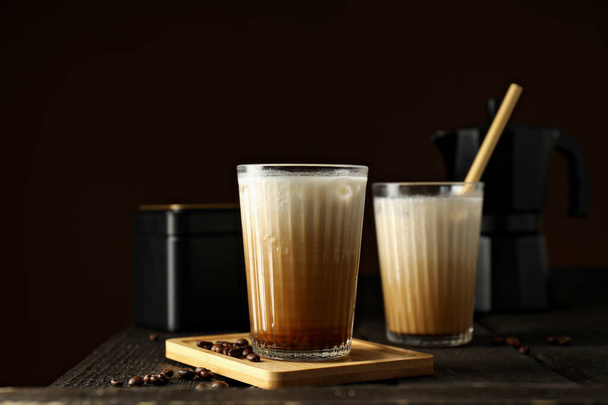 Lunettes avec café glacé, cafetière et grains de café sur fond brun foncé, gros plan - Photo, image