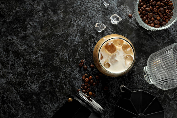 Vidrio con café helado, cafetera y grano de café sobre fondo gris, espacio para texto - Foto, Imagen
