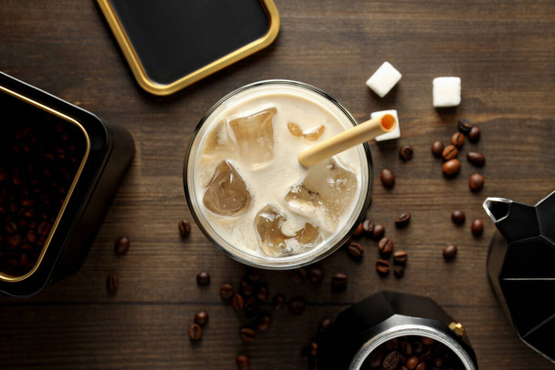Verre avec boisson glacée, cafetière, grains de café et sucre sur fond en bois, vue sur le dessus - Photo, image