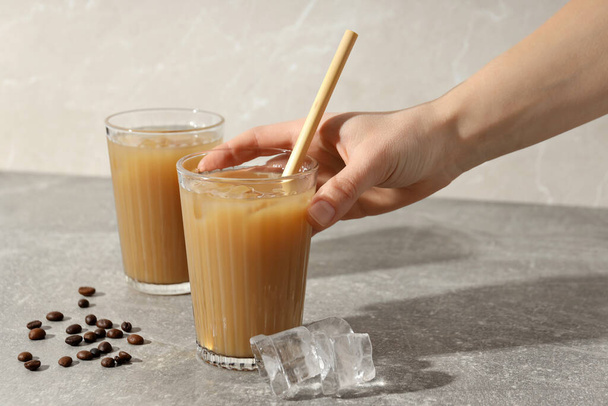Szemüveg jeges kávéval a kezében, jégkocka és kávébab szürke alapon - Fotó, kép