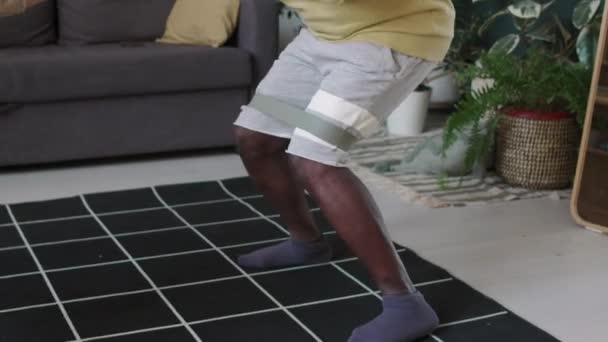 Orta yaşlı siyahi bir adamın antrenman sırasında bantlı basamak çömelme hareketi. - Video, Çekim