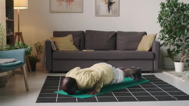 Szúrt lövés aktív idős fekete férfi csinál push-up a szőnyegen, miközben a beltéri sport edzés otthon - Felvétel, videó