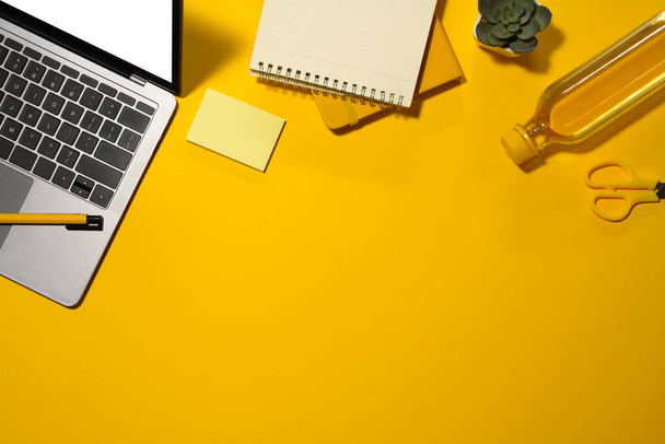 Laptop with empty screen, notepad and water bottle on yellow background. Top view with copy space. - Photo, Image