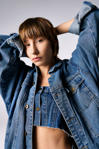 Una mujer joven y elegante con el pelo corto golpeando una pose segura mientras usa una chaqueta de jean en un entorno de estudio. - Foto, Imagen