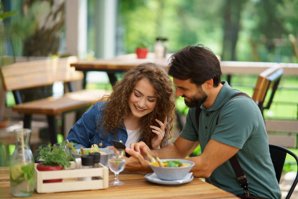 Young couple at date in restaurant, sitting on restaurant terrace. Boyfriend and girlfriend enjoying springtime, having lunch or brunch outdoors, outdoor seating for dining. - 写真・画像