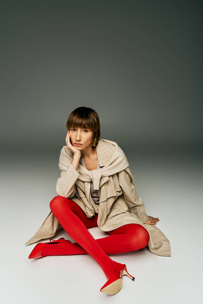 短い髪の若い女性が床に優雅に座り,スタジオの設定で活気に満ちた赤いタイツを着ています. - 写真・画像