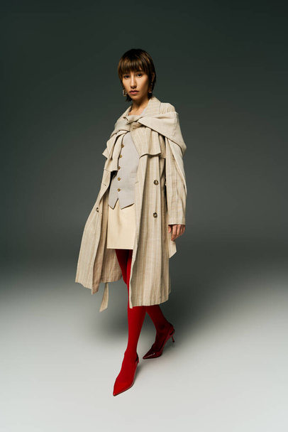 Stylowa młoda kobieta w płaszczu przedstawia swój niepowtarzalny styl z przyciągającymi wzrok czerwonymi rajstopami w studio. - Zdjęcie, obraz