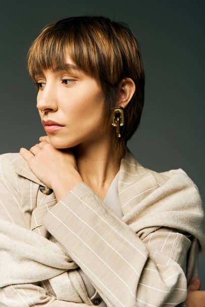 Una mujer joven y elegante con el pelo corto posa con confianza en un abrigo de moda en un entorno de estudio. - Foto, imagen