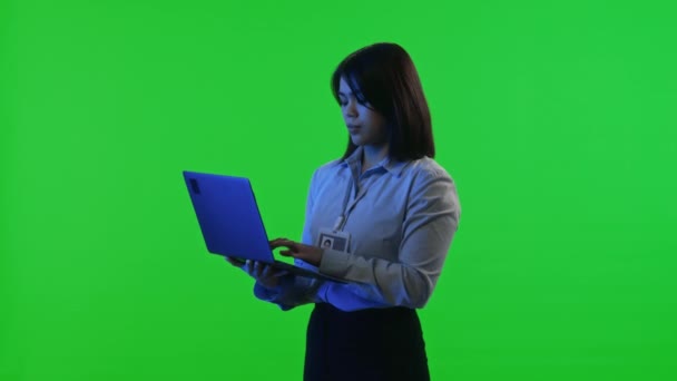 女性のデータセンターエンジニアは,緑色のクロマキー画面に対して青いネオンライトの下に立っている間,ラップトップにタイピングバッジとフォーマルウェアを着用します - 映像、動画