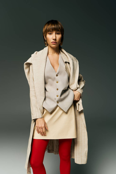 Uma jovem elegante com cabelo curto posa em collants e um casaco em um ambiente de estúdio, exalando confiança e elegância. - Foto, Imagem