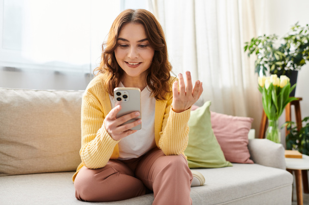 A middle-aged woman seated on a couch, holding a cellphone. - Photo, Image