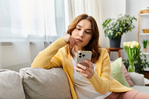 Женщина, сидящая на диване, поглощенная своим телефоном. - Фото, изображение