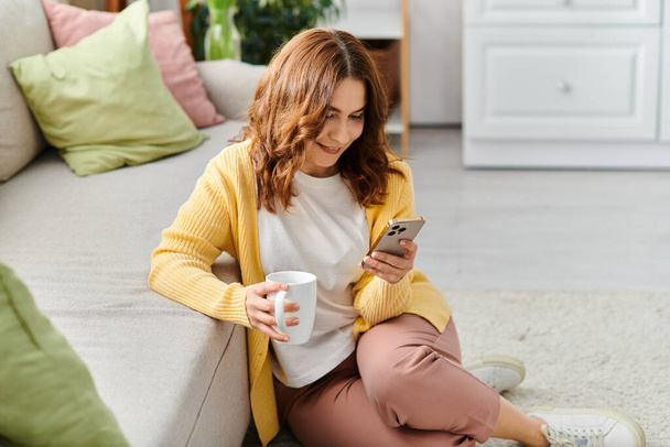 Eine Frau mittleren Alters in ihr Handy vertieft, während sie auf einer Couch sitzt. - Foto, Bild