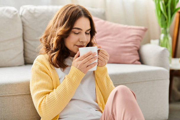 Μεσήλικη γυναίκα απολαμβάνει μια στιγμή με καφέ σε ένα άνετο καναπέ. - Φωτογραφία, εικόνα