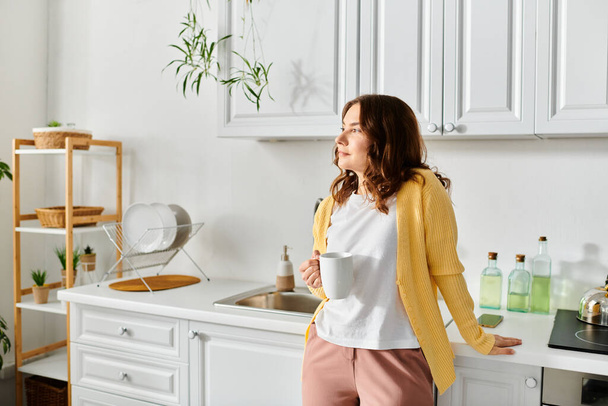 Žena středního věku klidně stojí v kuchyni a drží šálek. - Fotografie, Obrázek
