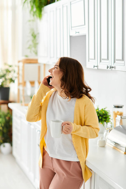 Жінка середнього віку, що стоїть на кухні, спілкується на мобільному телефоні. - Фото, зображення