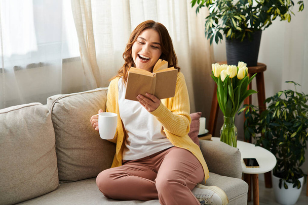 Mujer de mediana edad absorto en un libro mientras está sentado en un sofá acogedor. - Foto, imagen