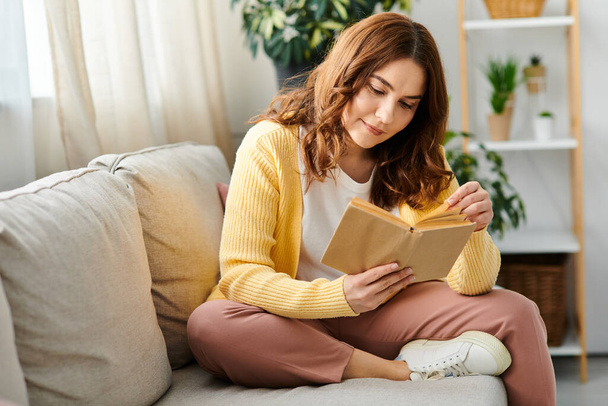 Жінка середнього віку мирно поглинула читання, сидячи на дивані. - Фото, зображення