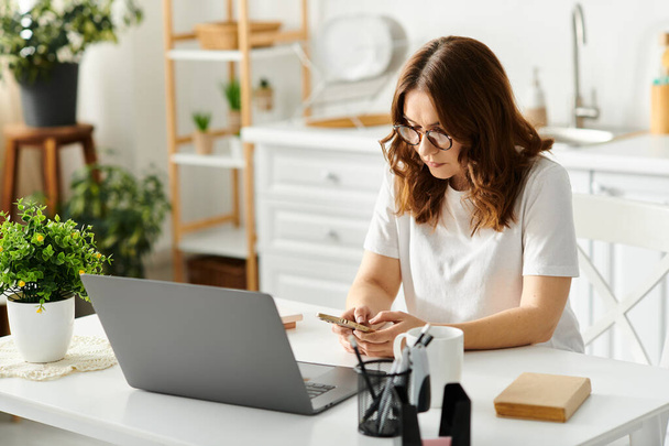 Uma mulher de meia-idade sentada em uma mesa, absorvida em usar um computador portátil. - Foto, Imagem